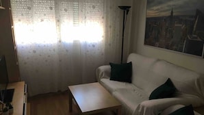 A living room with a sofa, a coffee table, a lamp, and a cityscape painting on the wall. - AVE station at 10 min walking - Sostoa Apartment (Málaga)