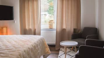 A hotel room with a bed, a seating area with a table, and a window with curtains.