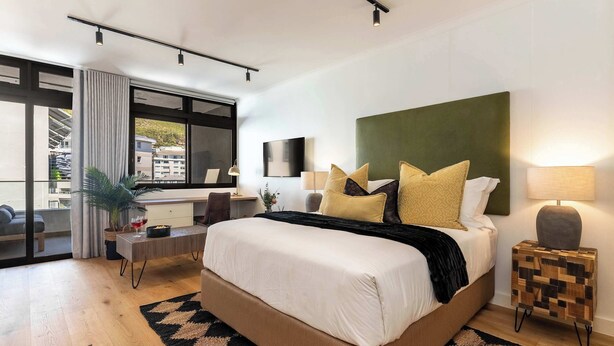 A modern bedroom with a large bed, a desk, a chair, a TV, and a window with a view of buildings. - Views, BBQ, Balcony, Sea Point - Jade Views Studio (Cape Town)