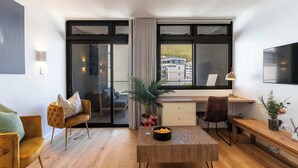 A modern living room with a wooden coffee table, a sofa, a desk, and a TV. - Views, BBQ, Balcony, Sea Point - Jade Views Studio (Cape Town)