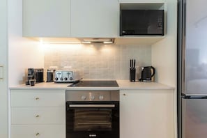 Eine moderne Küche mit weißen Schränken, einem Bosch-Ofen, einer Mikrowelle und einem Edelstahl-Kühlschrank.