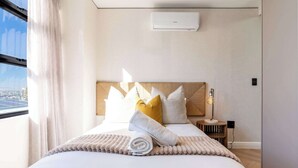 A hotel room with a bed, pillows, a bedside table, a lamp, and a window with curtains. - Stunning Views, Duplex, Bo-Kaap - Aerie Penthouse (Cape Town)