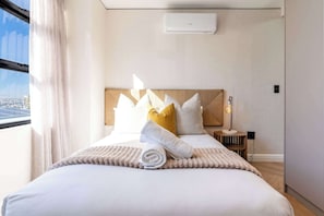 A hotel room with a bed, pillows, a bedside table, a lamp, and a window with curtains. - Stunning Views, Duplex, Bo-Kaap - Aerie Penthouse (Cape Town)