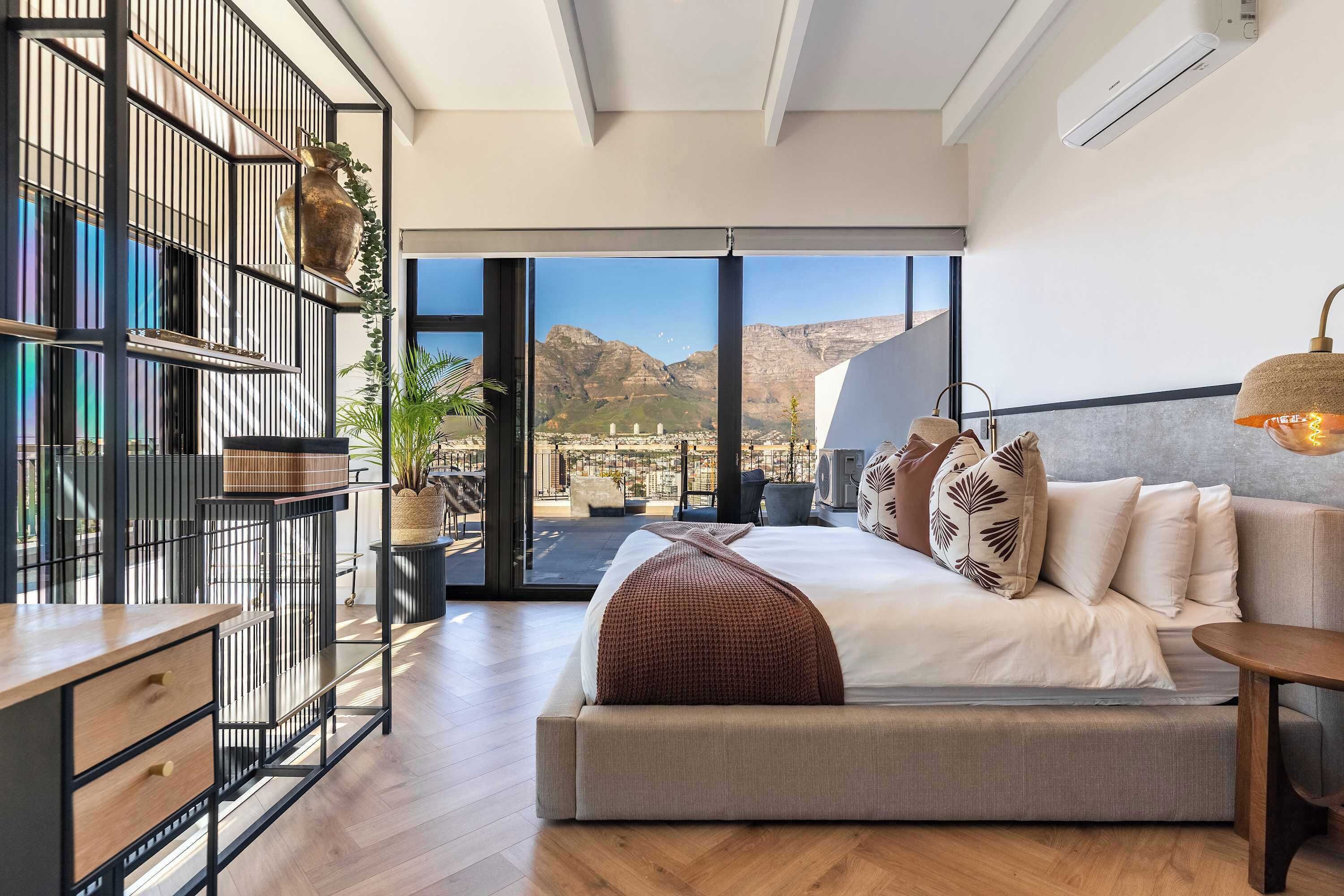 A modern bedroom with a large bed, a desk, and a view of mountains through a sliding door.