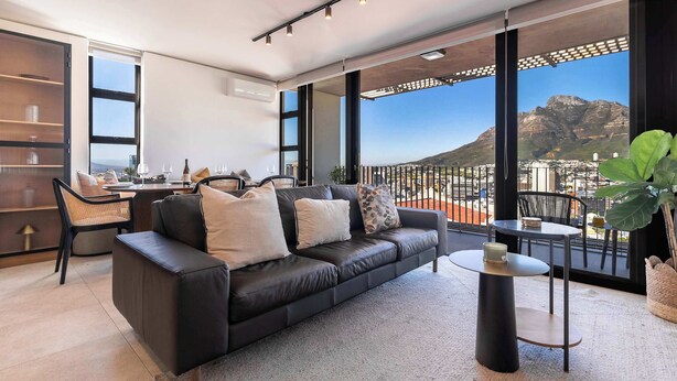 A modern living room with a leather sofa, a coffee table, and a view of a mountain. - Stunning Views, Duplex, Bo-Kaap - Aerie Penthouse (Cape Town)