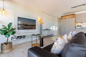 A modern living room with a flat-screen TV, a large potted plant, a leather sofa, and a minimalist coffee table. - Stunning Views, Duplex, Bo-Kaap - Aerie Penthouse (Cape Town)