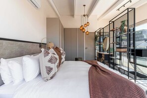 Une chambre d’hôtel moderne avec un grand lit, un bureau, une chaise, un luminaire suspendu et une vue sur l’extérieur.