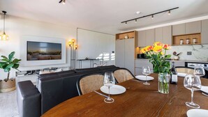 A modern dining area with a wooden table, chairs, and a television mounted on the wall. - Stunning Views, Duplex, Bo-Kaap - Aerie Penthouse (Cape Town)