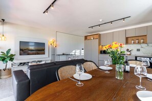 A modern dining area with a wooden table, chairs, and a television mounted on the wall. - Stunning Views, Duplex, Bo-Kaap - Aerie Penthouse (Cape Town)