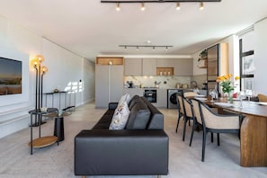 Une cuisine moderne dotée d’appareils électroménagers intégrés, un coin repas avec une table et des chaises en bois, et un salon avec un canapé et une table basse.