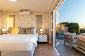 Ein Schlafzimmer mit Bett, Nachttischen, einer Lampe, einem Fenster und einem Balkon mit Pool.