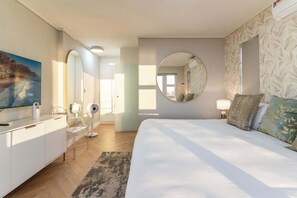 Ein Schlafzimmer mit einem Bett, einem Schminktisch, einem Spiegel, einem Fernseher und einem Fenster.