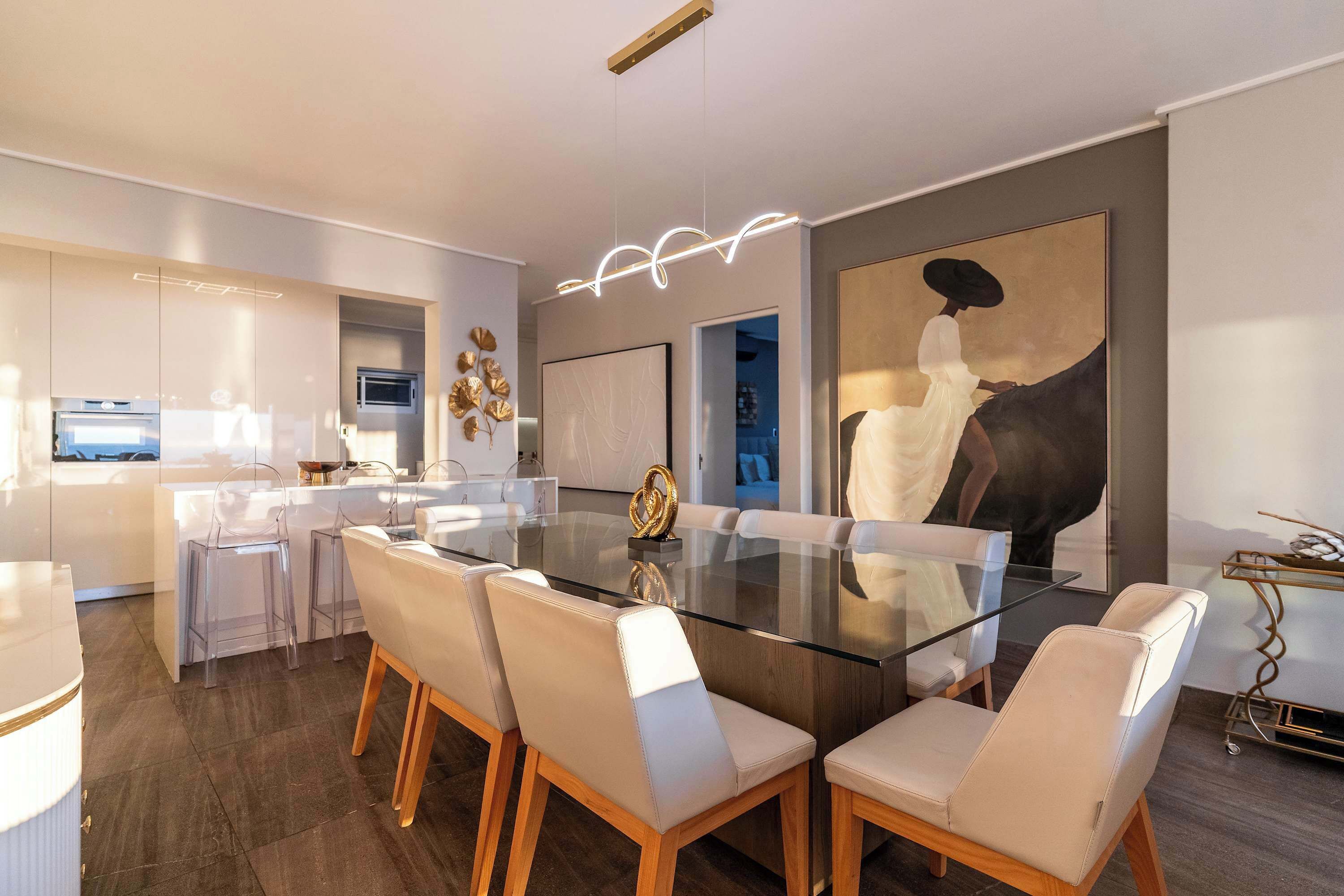 A modern dining area with a glass table, white chairs, and a contemporary light fixture.