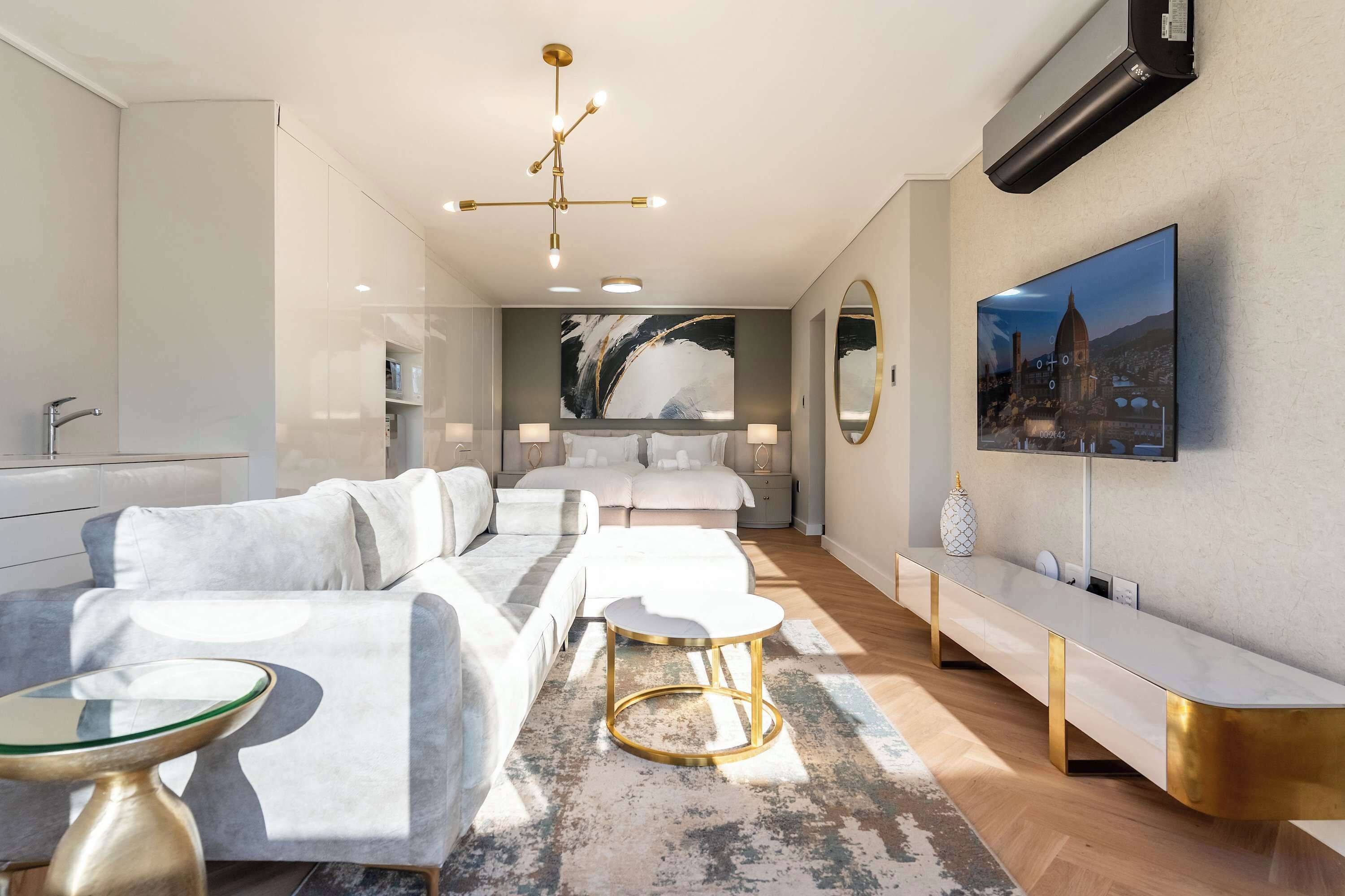 A modern hotel room with a sofa, a round table, a large painting, and a TV mounted on the wall.