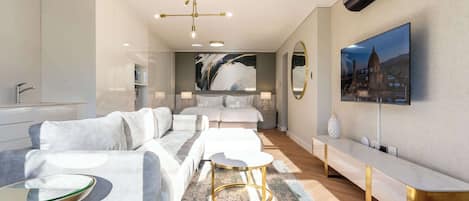 A modern hotel room with a sofa, a round table, a large painting, and a TV mounted on the wall.