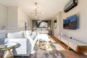Ein modernes Hotelzimmer mit einer Couch, einem runden Tisch, einem großen Gemälde und einem an der Wand befestigten Fernseher.