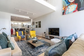 A modern living room with a sofa, armchairs, a coffee table, and a TV. - Modern & Artistic, Green Point - Urban Palette Apt (Cape Town)