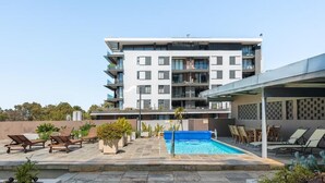 Een modern appartementencomplex met een zwembad op het dak, lounge stoelen en potplanten.