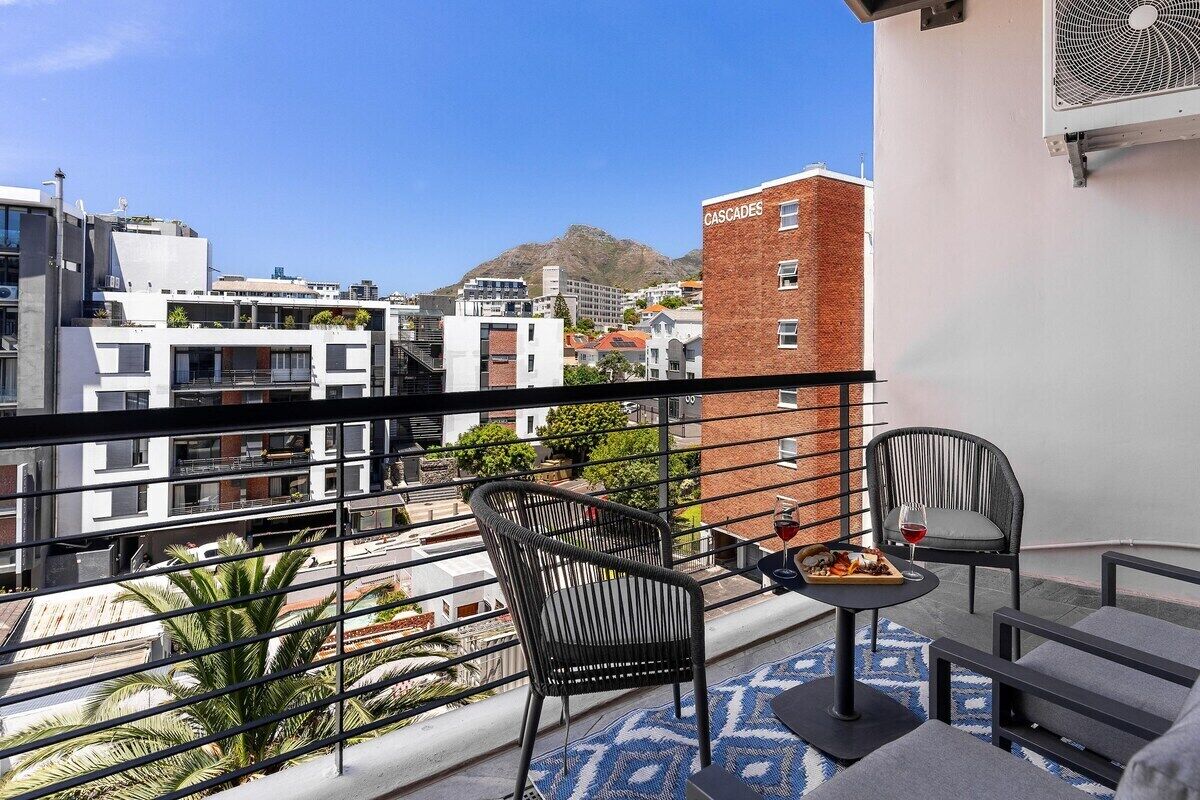 A balcony with two chairs, a table, and a view of a cityscape with a mountain in the background.