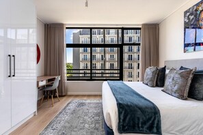 A modern bedroom with a large window, a desk, and a bed with multiple pillows. - Modern & Artistic, Green Point - Urban Palette Apt (Cape Town)