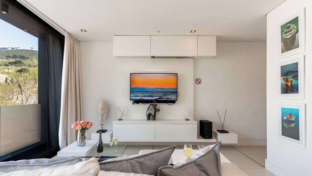 A modern living room with a large window, a flat-screen TV, a white sofa, and a minimalist decor style. - Views, De Waterkant CPT, Communal Pool -901 Mirage (Cape Town)