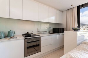 A modern kitchen with white cabinets, a built-in oven, and a window with a view of a cityscape. - Views, De Waterkant CPT, Communal Pool -901 Mirage (Cape Town)