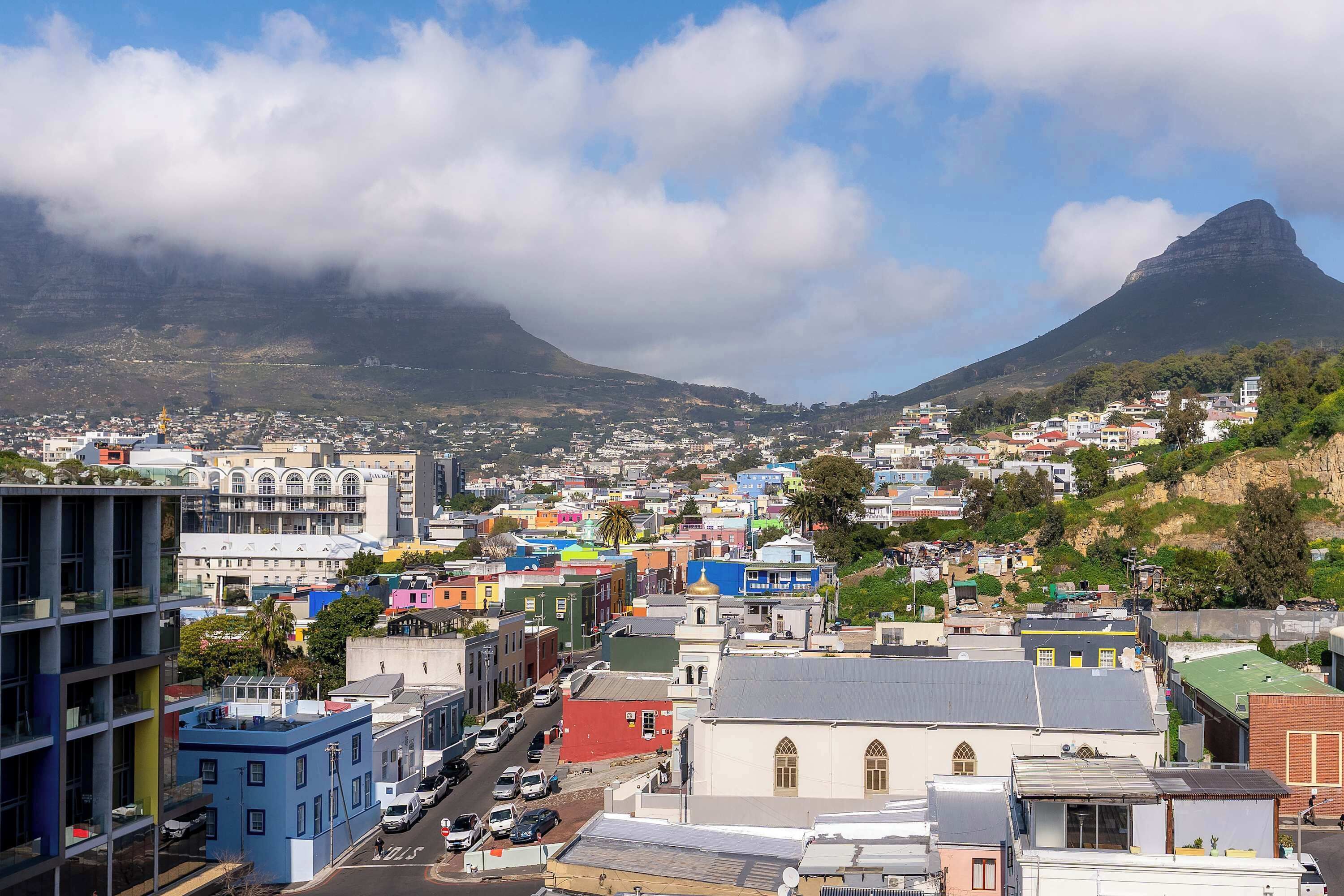 A cityscape with a prominent mountain in the background, colorful buildings, and a clear sky.
