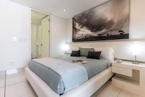 A modern bedroom with a large bed, bedside tables, and a painting of a cloudy sky. - Views, De Waterkant CPT, Communal Pool -901 Mirage (Cape Town)