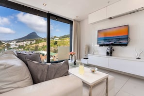 A modern living room with a large window, a flat-screen TV, and a sofa. - Views, De Waterkant CPT, Communal Pool -901 Mirage (Cape Town)