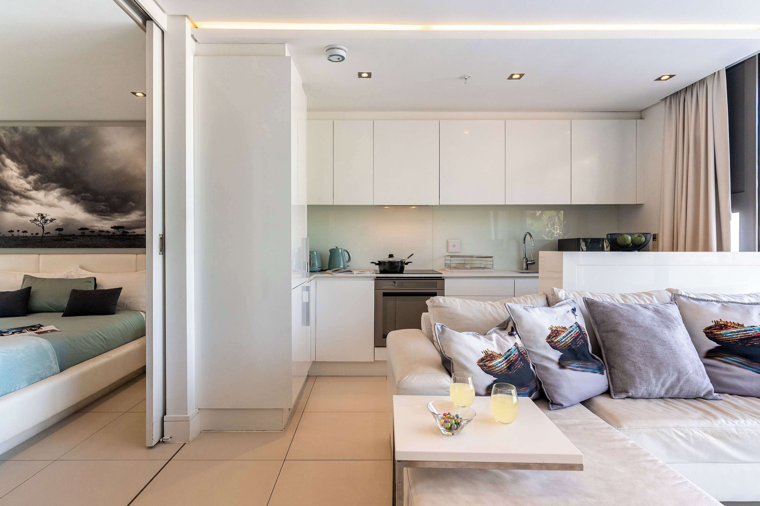 A modern living room with a sofa, a coffee table with drinks, and a kitchen in the background.