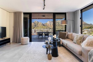 A modern living room with a large window offering a mountain view, a sofa, a coffee table, and a TV. - Modern, Gorgeous Views, Bo-Kaap - Vista Luxe Apt (Cape Town)