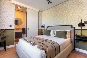 A modern bedroom with a large bed, a bedside table with a lamp, a mirror, and a bathroom visible through an open door. - Modern, Gorgeous Views, Bo-Kaap - Vista Luxe Apt (Cape Town)