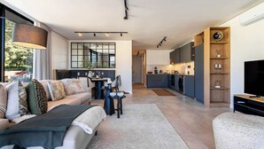 Una sala de estar moderna con sofá, mesa de centro y televisor. Se ve una cocina al fondo, junto con un comedor.