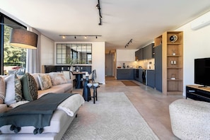 A modern living room with a sofa, coffee table, and a TV. A kitchen is visible in the background with a dining area. - Modern, Gorgeous Views, Bo-Kaap - Vista Luxe Apt (Cape Town)