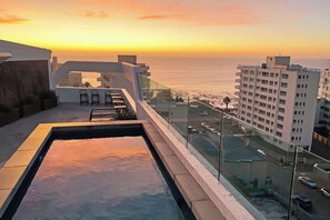 Ein Dachpool mit Blick auf den Sonnenuntergang über dem Meer, angrenzende Gebäude und einen klaren Himmel.