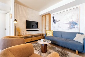 Ein modernes Wohnzimmer mit einem blauen Sofa, einem runden Couchtisch und einem flachbildfernseher an der Wand.