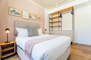 Ein Schlafzimmer mit einem großen Bett, Nachttischen und einem Kleiderschrank mit offenen Regalen.