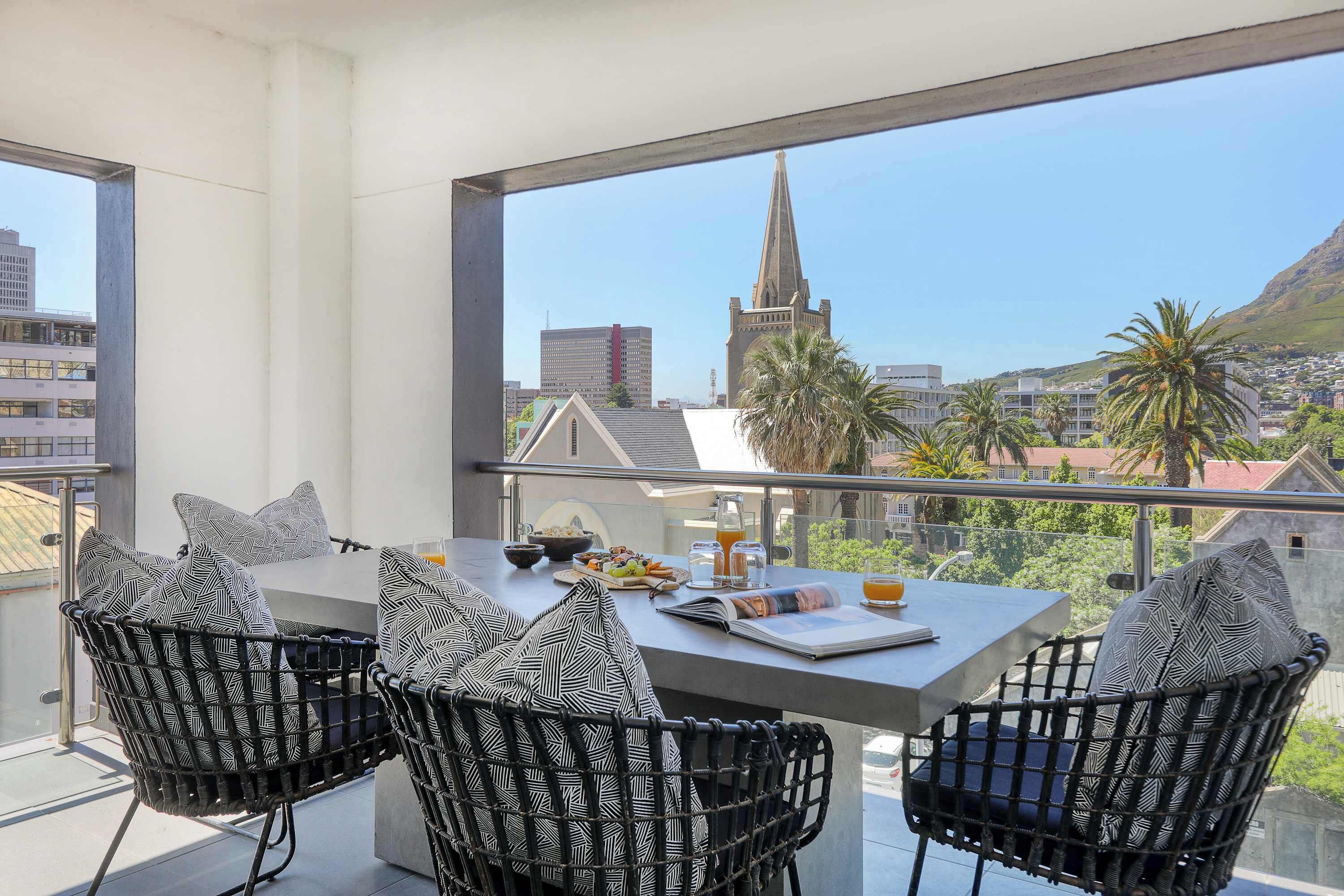 Un balcón con una mesa de comedor, sillas y vistas a la aguja de una iglesia y edificios.