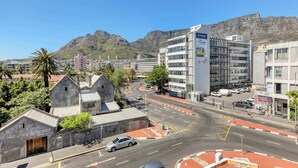 Eine Stadtansicht mit einem markanten Gebäude, das eine große Werbung zeigt, einer Kreisverkehr und einem Berg im Hintergrund.