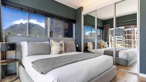 Ein modernes Schlafzimmer mit einem großen Bett, einem Nachttisch, einem Spiegel und Blick auf Berge durch große Fenster.