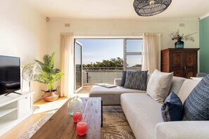 Ein Wohnzimmer mit einer Couch, einem Fernseher, einer Pflanze und einem Balkon mit Blick.