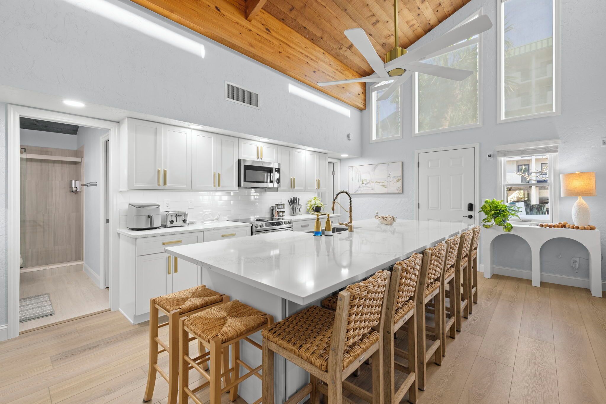 A modern kitchen with white cabinetry, a large island, and a ceiling fan.
