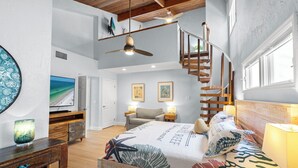 Une chambre spacieuse avec un grand lit, un plafond en bois, un téléviseur intégré et un escalier menant à un niveau supérieur.