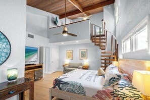 Un'ampia camera da letto con un letto grande, soffitto in legno, TV integrata e una scala che conduce a un livello superiore.