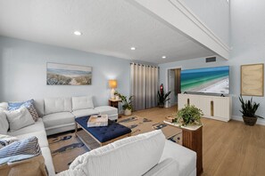Een moderne woonkamer met een bank, poef en een flatscreen televisie.