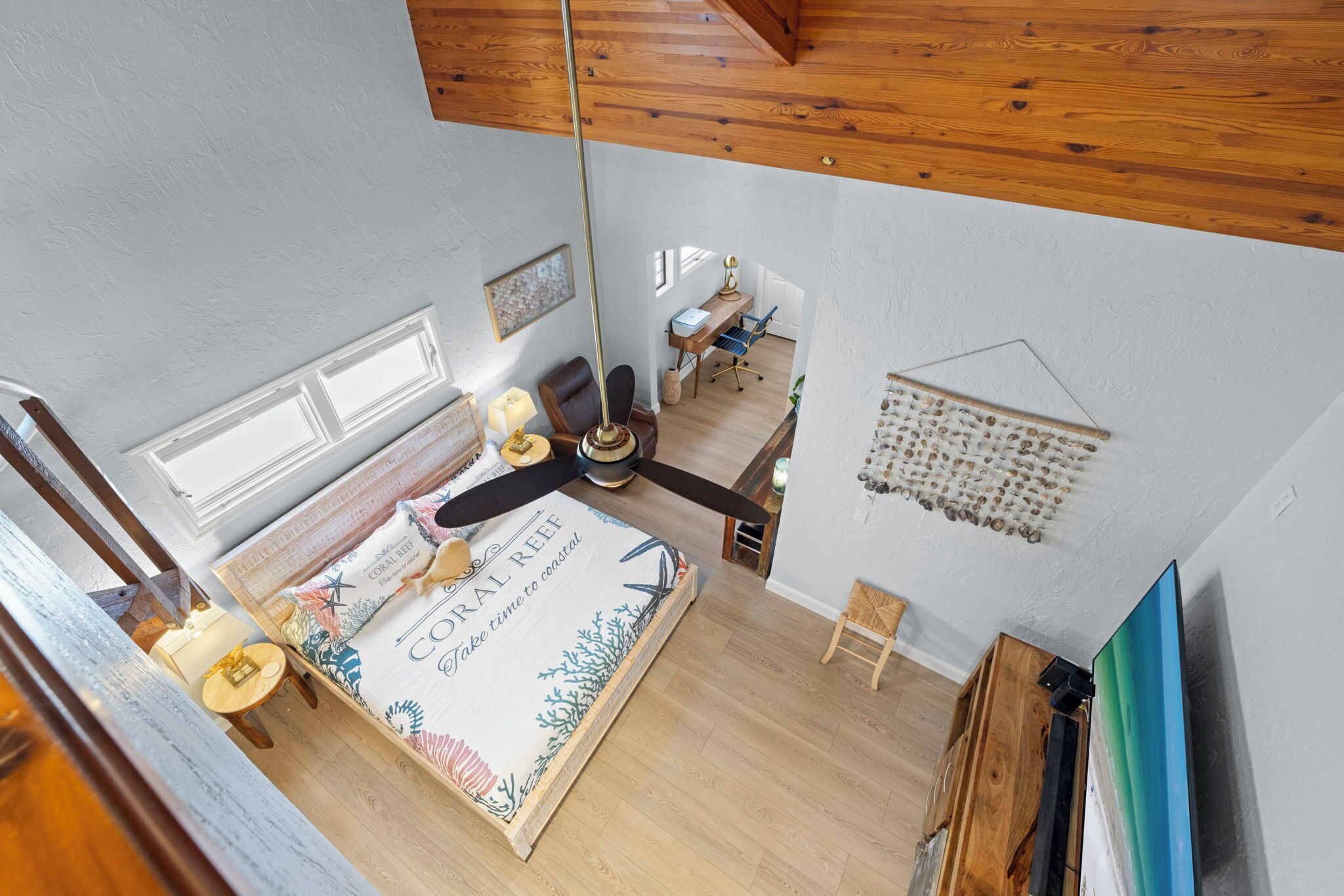 A bedroom with a bed, a desk, a chair, a ceiling fan, and a wall-mounted light fixture.