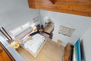 A bedroom with a bed, a desk, a chair, a ceiling fan, and a wall-mounted light fixture.