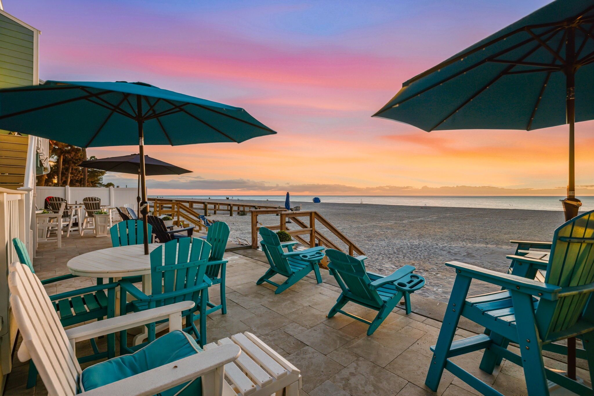 An outdoor seating area with tables and chairs, overlooking a beach and the ocean.