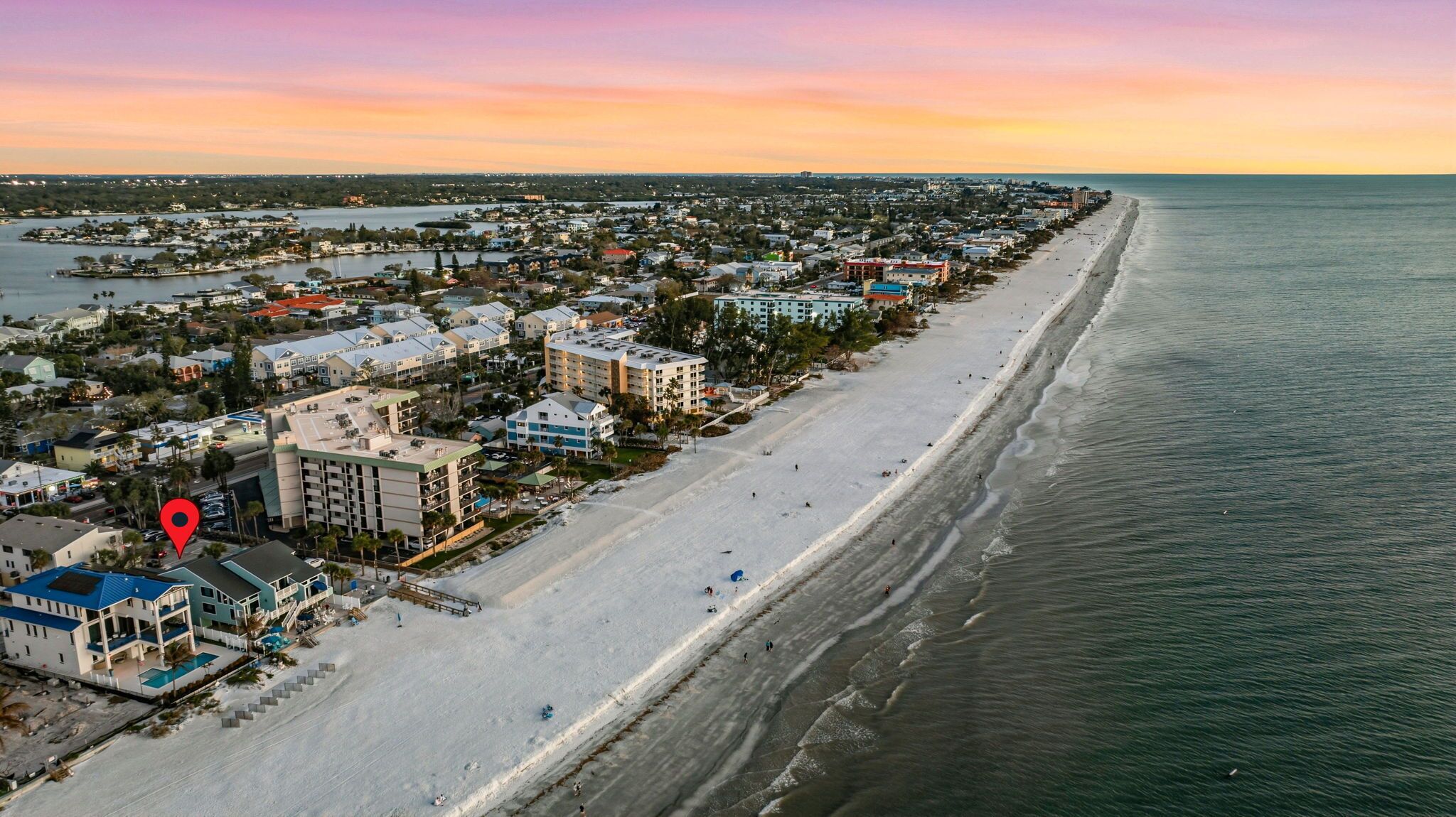 Un pueblo costero con una extensa playa, edificios residenciales y un puerto deportivo.