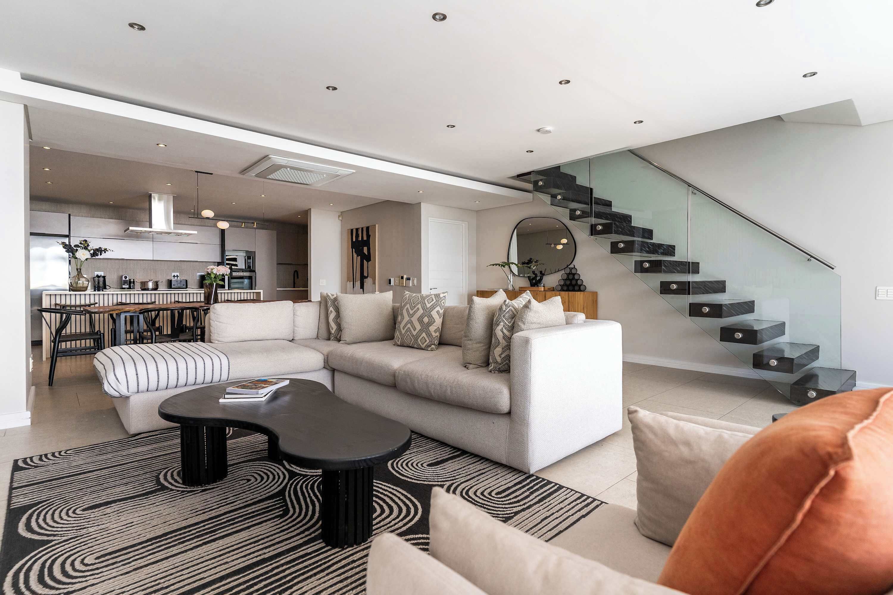 Un salon moderne avec un canapé d’angle, une table basse et un escalier doté de rampes en verre.